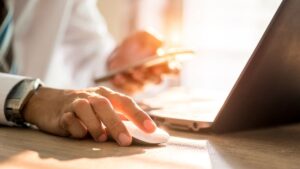 hands using a computer mouse and smartphone in front of computer