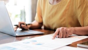 Person using laptop and checking a sheet of printed PPC analytics