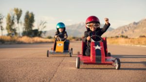 two children in soap box racers on a road having a race