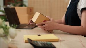 small business owner preparing merchandise to be posted while using a laptop